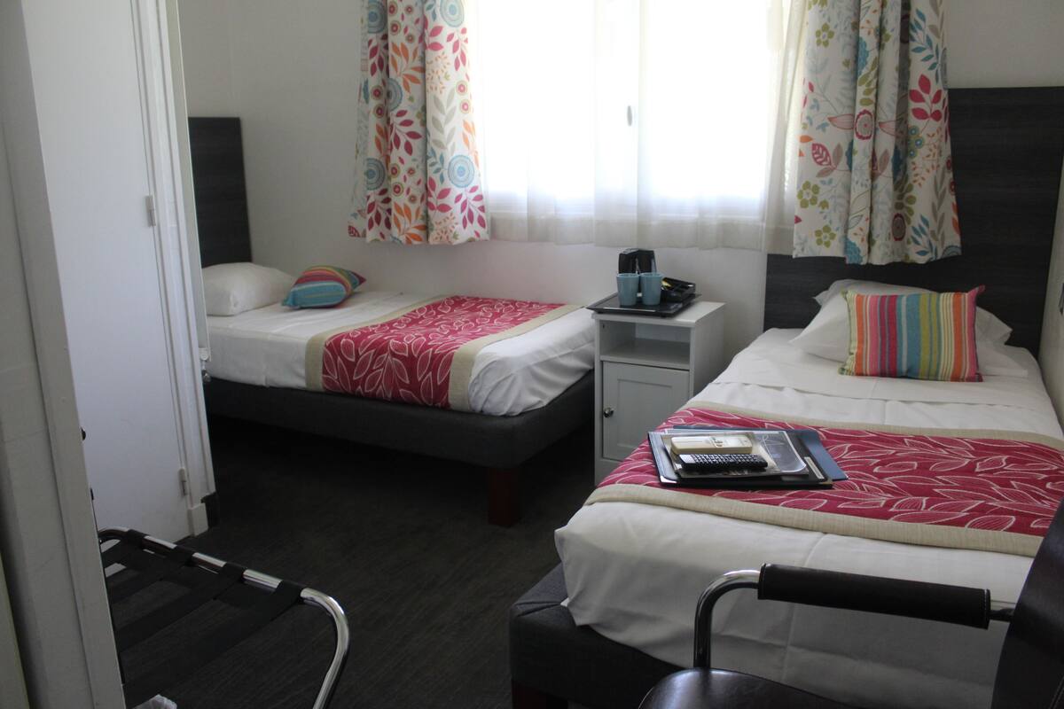 A hotel room with two beds, a small table with a phone and a coffee maker, and a chair.
