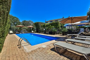 A swimming pool with lounge chairs and umbrellas, surrounded by greenery and a clear blue sky. - Hotel des Cayrons (Vence)