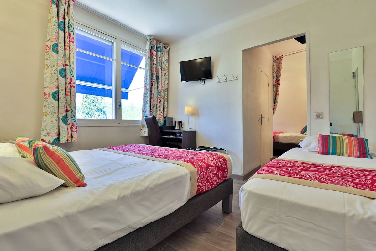 A hotel room with two beds, a desk with a chair, a TV, and a door leading to another room.