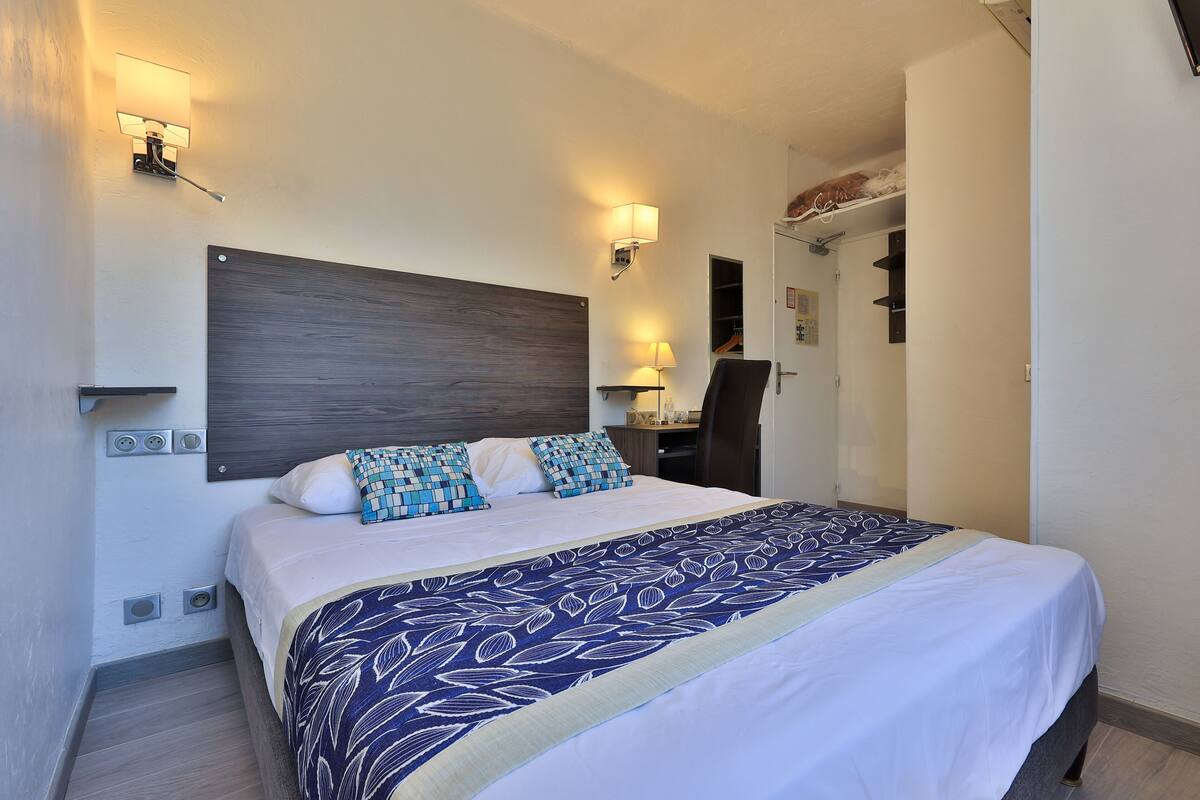 A neatly made bed with a patterned bedspread, two wall-mounted lamps, and a wooden headboard.