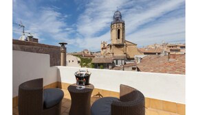 A rooftop terrace with wicker furniture and a table with a candle holder. In the background, there is a church with a bell tower. - Hotel des Augustins (Aix-en-Provence)