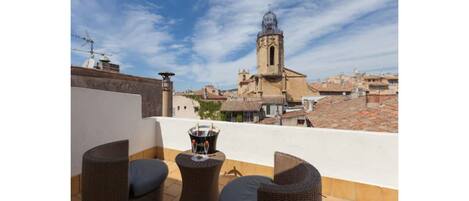 A rooftop terrace with wicker furniture and a table with a candle holder. In the background, there is a church with a bell tower.