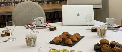 Una mesa de conferencias con pasteles, una computadora portátil y una pizarra blanca en una sala con estanterías.