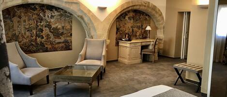 A hotel room with a bed, two armchairs, a small table, a desk with a chair, and a decorative wall with a mural.