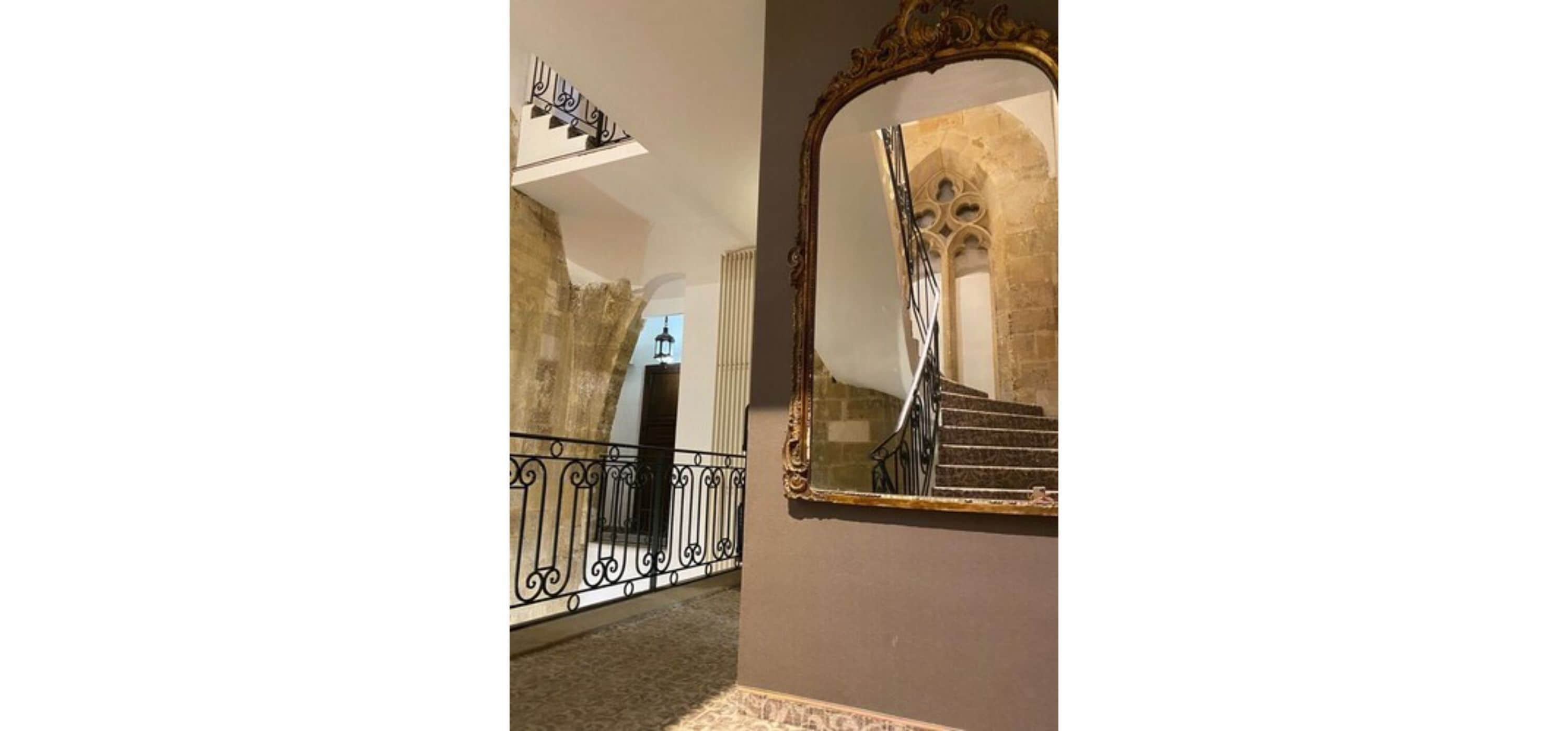 Eine Treppe mit schmiedeeisernem Geländer und einem Spiegel, der die Treppe widerspiegelt.