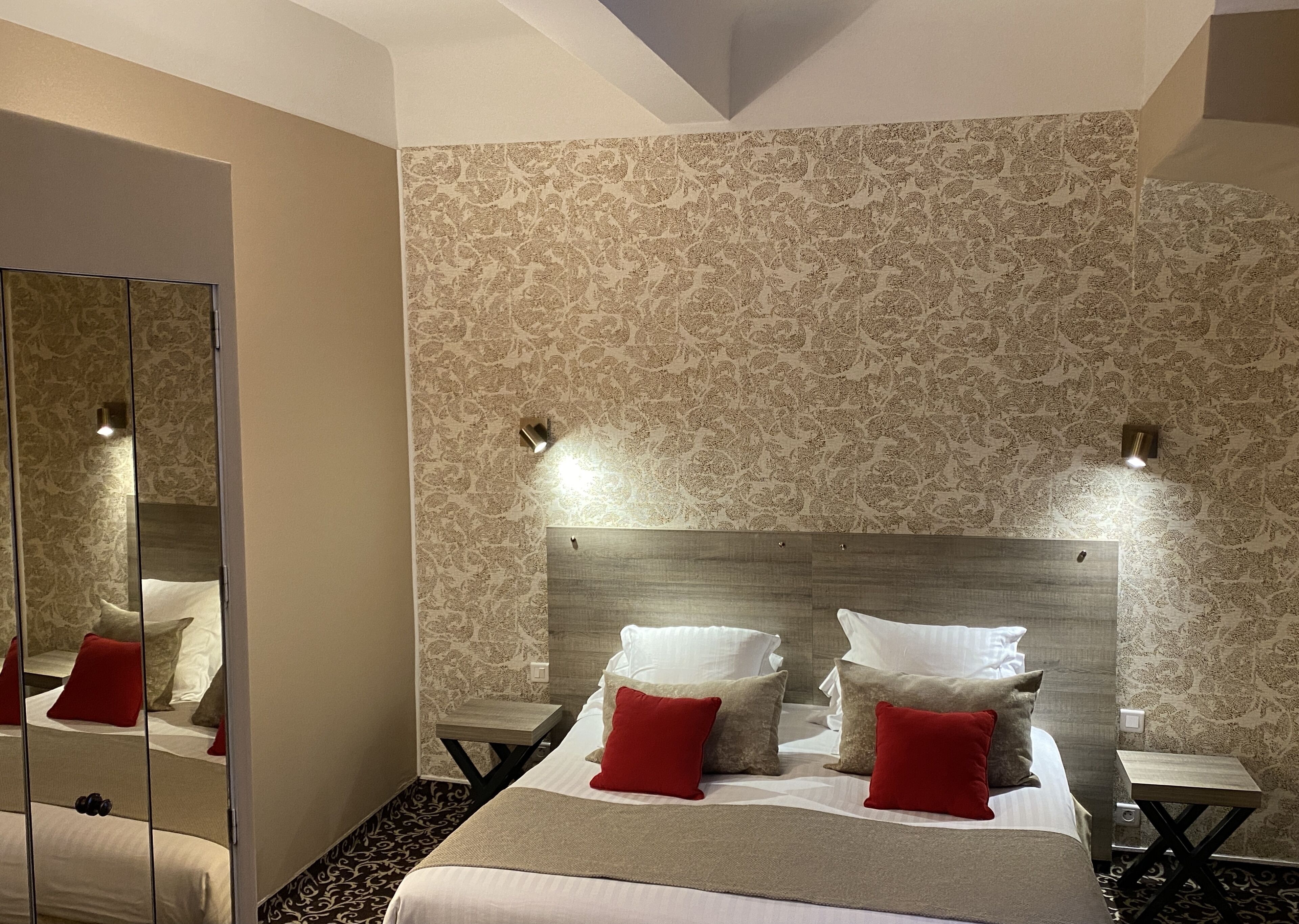 A hotel room with a large bed, two bedside tables, a mirror, and patterned wallpaper.