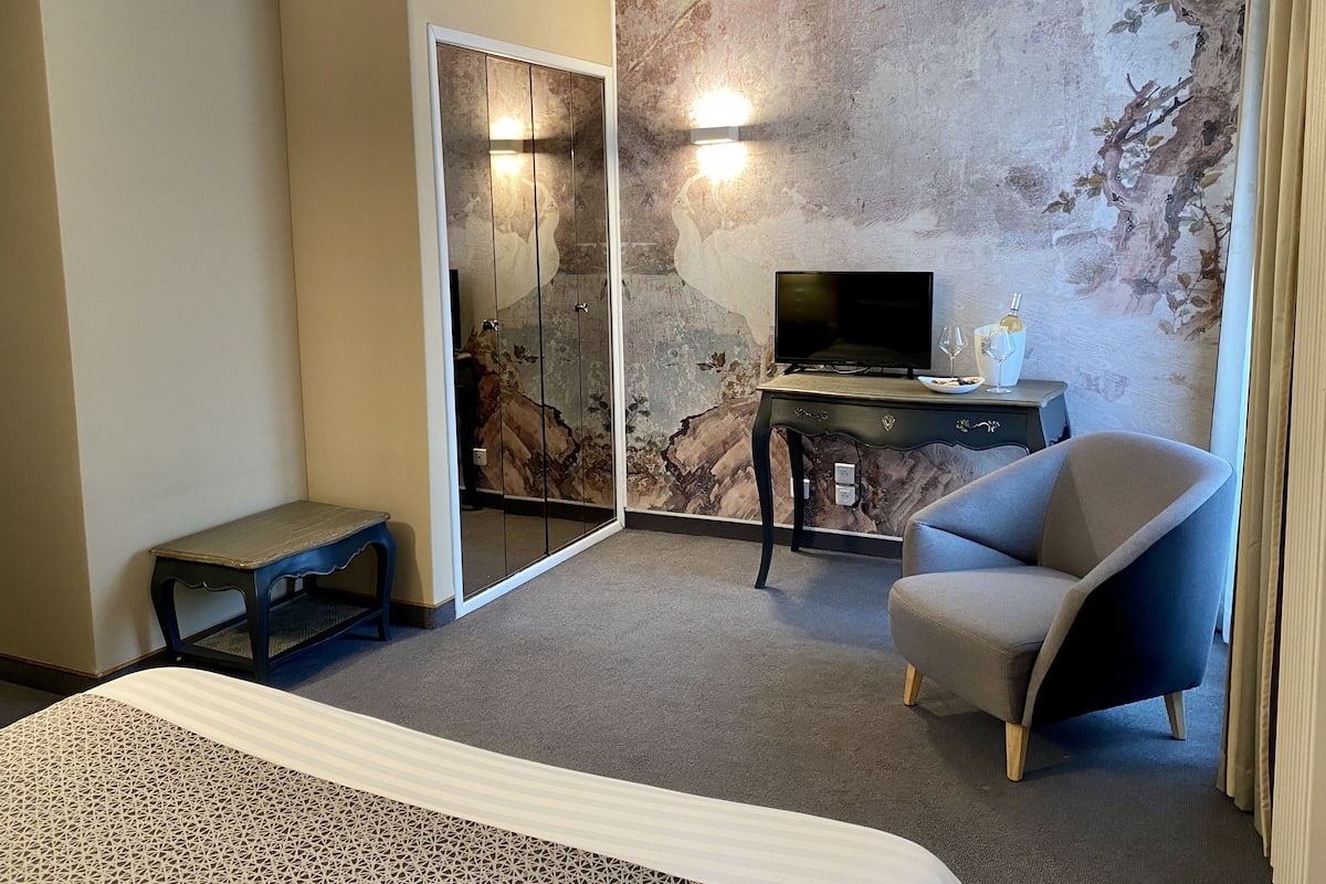 A hotel room with a bed, a desk with a TV, a chair, and a decorative wall.