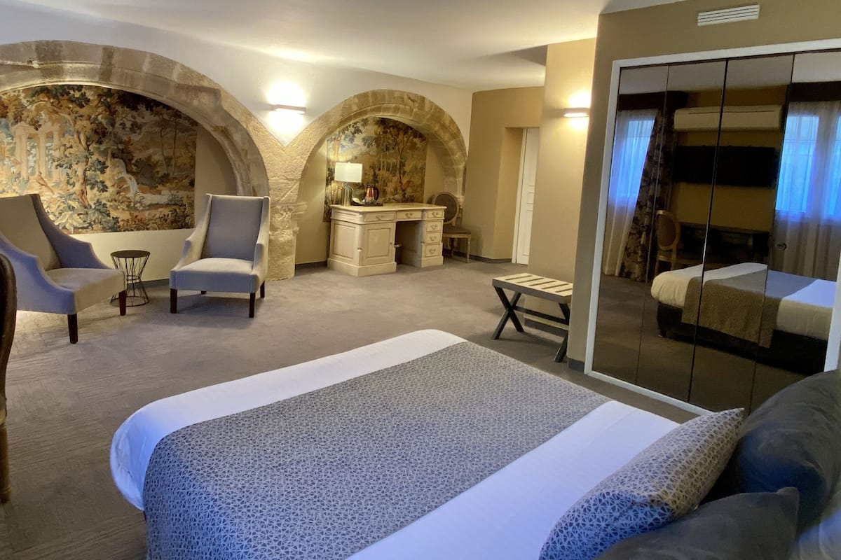 A hotel room with a large bed, two armchairs, a desk, and a mirror.