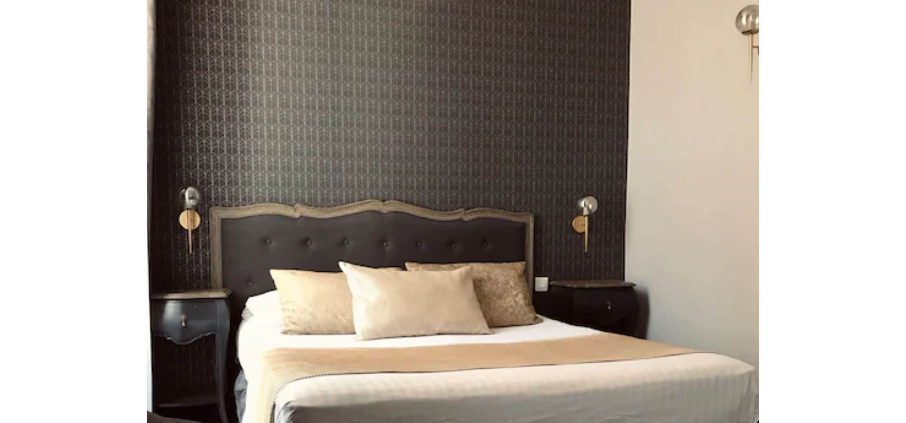 Een netjes opgemaakt bed met een gestoffeerd hoofdeinde, twee nachtkastjes en een structuurwand erachter.