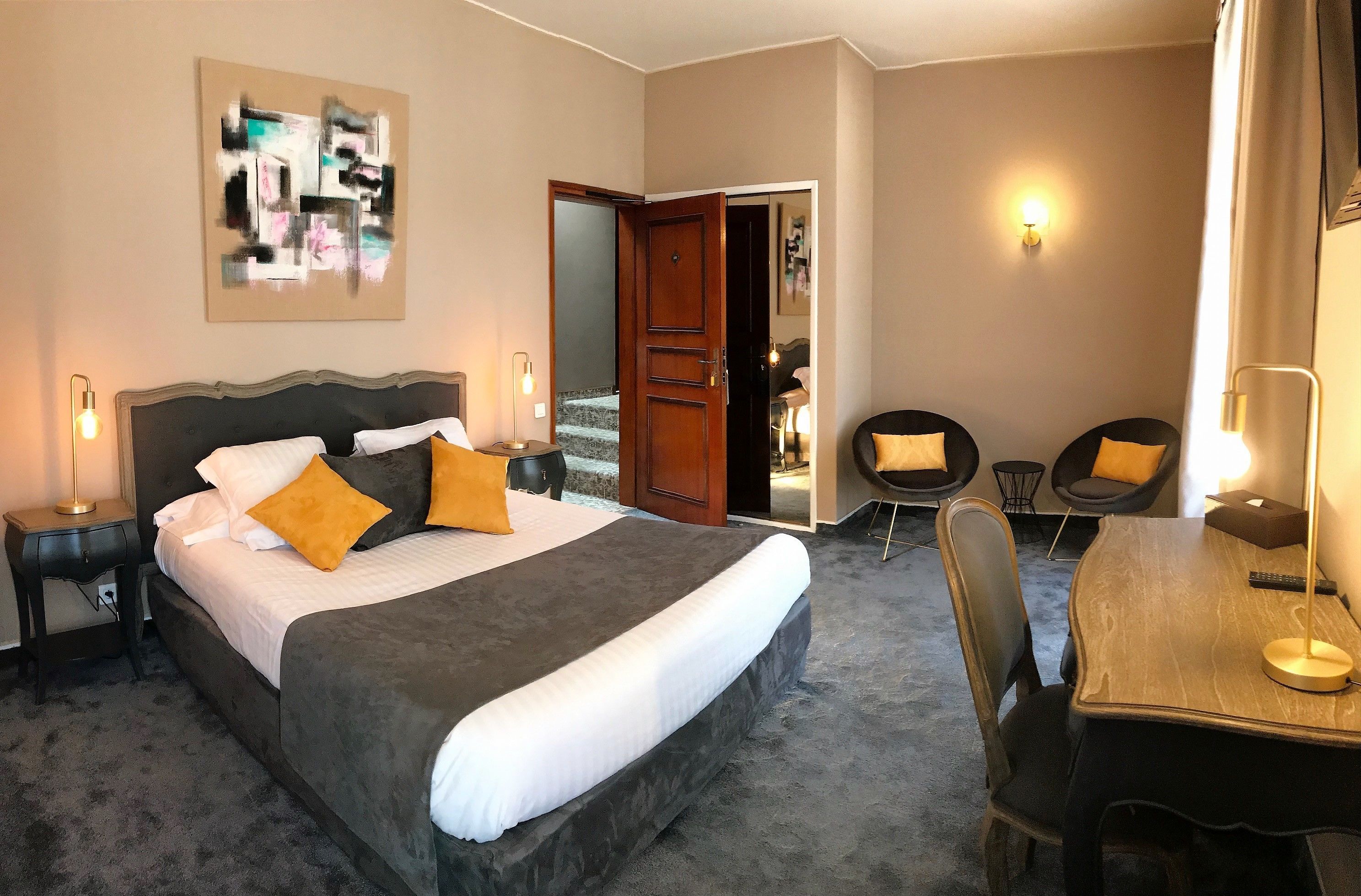 Une chambre d’hôtel avec un grand lit, un bureau, deux chaises, une porte donnant sur une salle de bain et une œuvre d’art accrochée au mur.