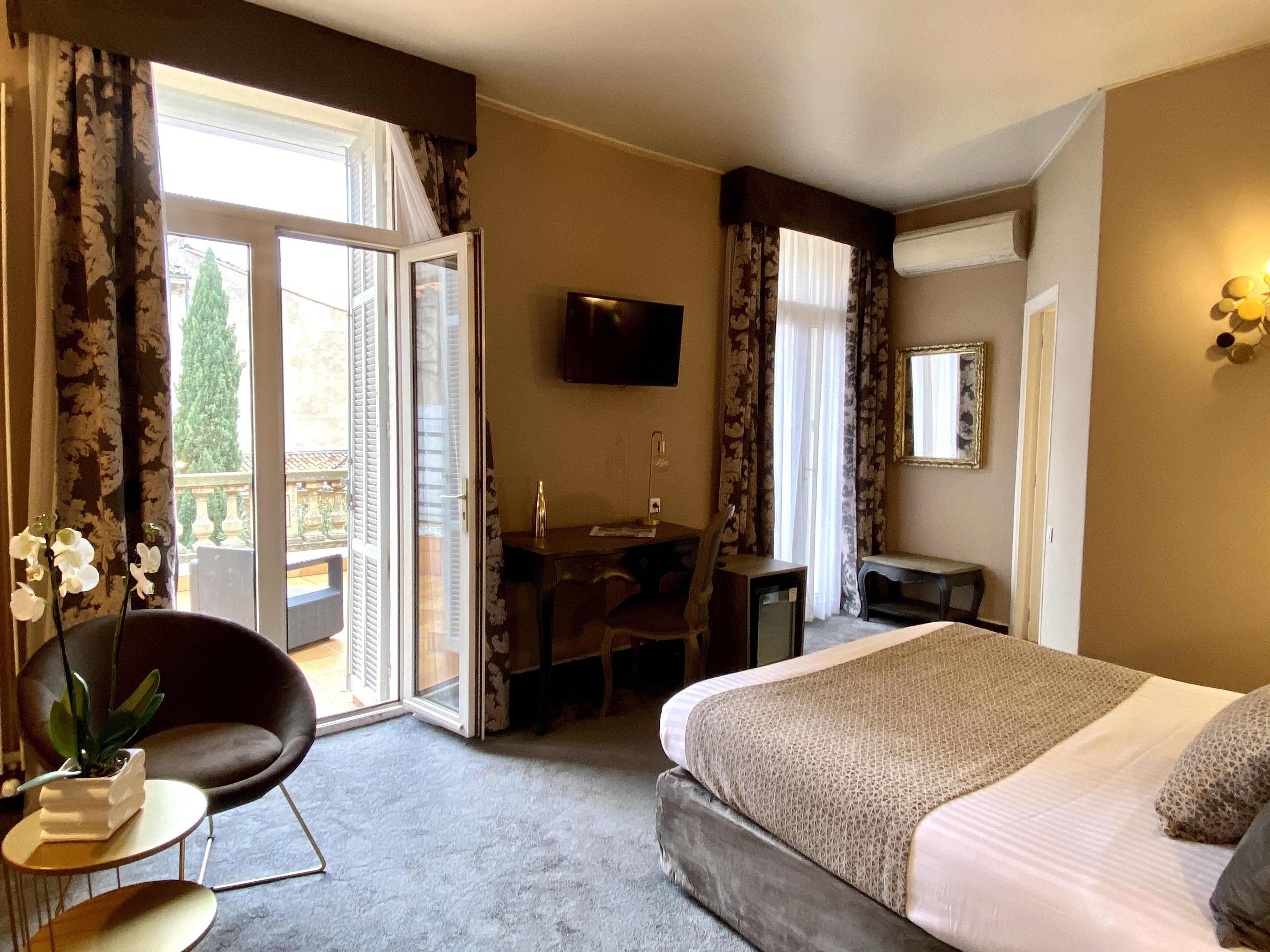 A hotel room with a bed, a desk, a chair, a TV, and a balcony with curtains.