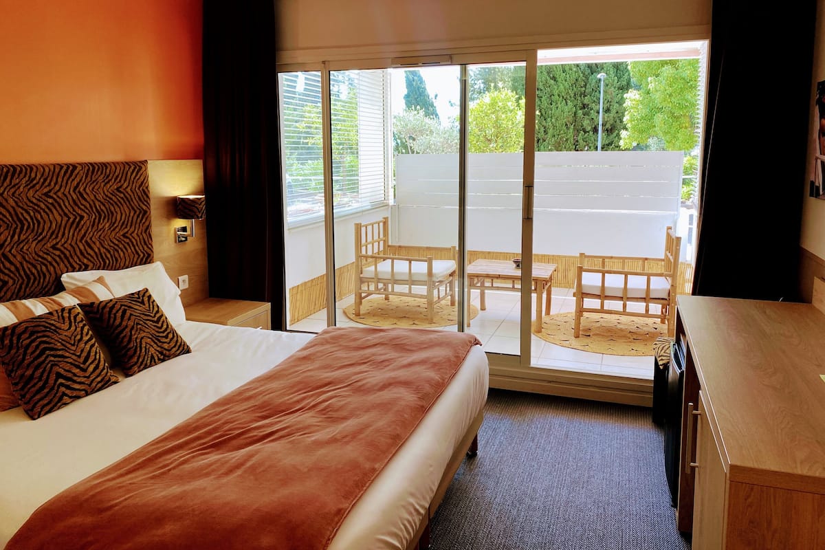 A hotel room with a bed, a desk, a chair, and a balcony with a view of the parking lot.