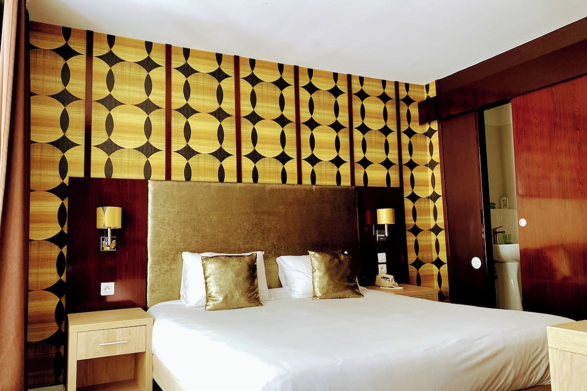 A hotel room with a large bed, wooden headboard, two bedside tables, and a mirror.
