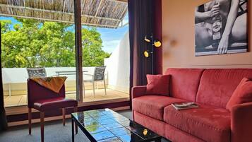 Ein rotes Sofa, ein Glastisch, ein Sessel, ein großes Fenster mit Blick auf Bäume und ein Bild an der Wand.