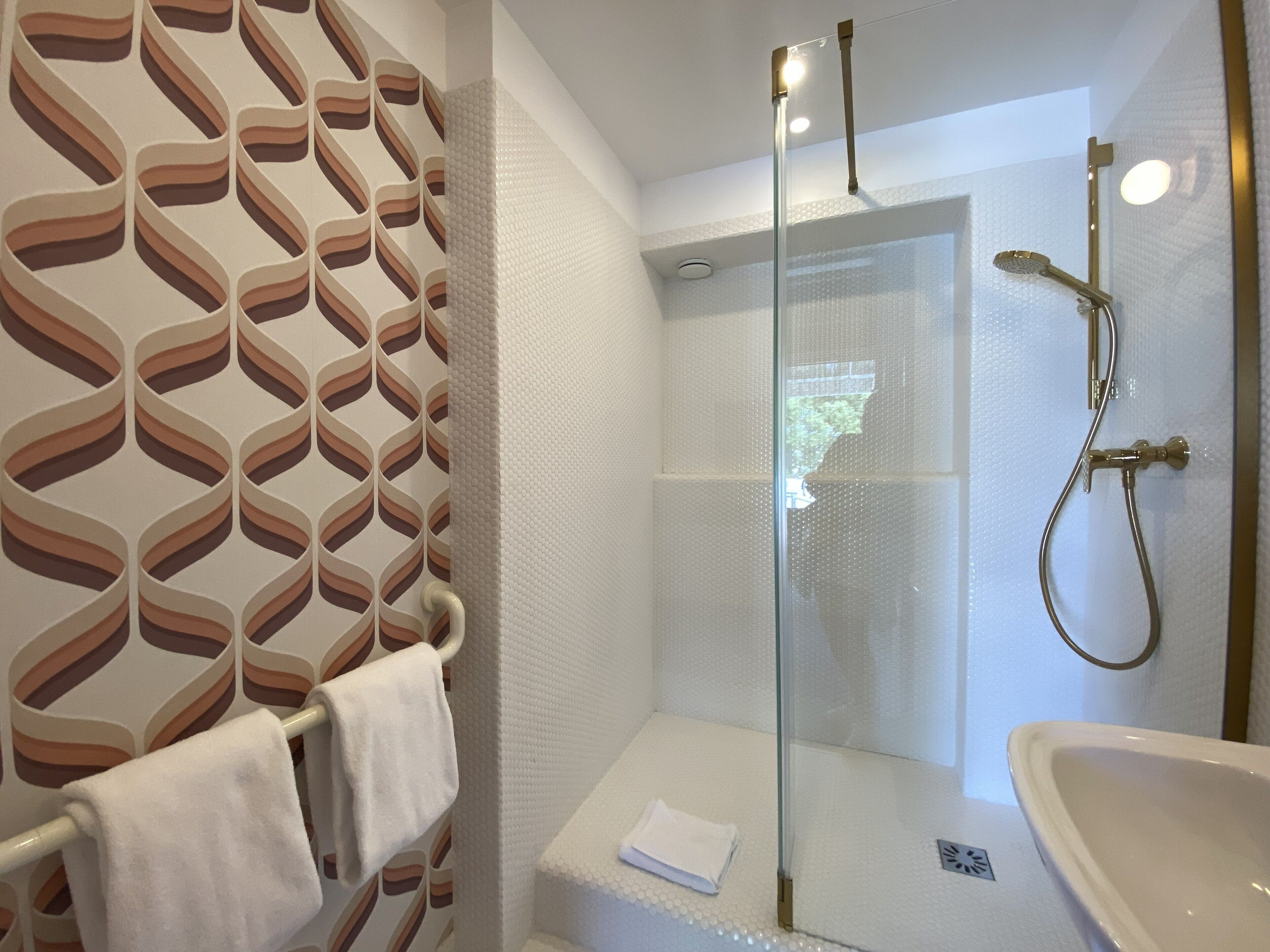 A modern bathroom with a glass-enclosed shower, a white sink, and a towel rack.