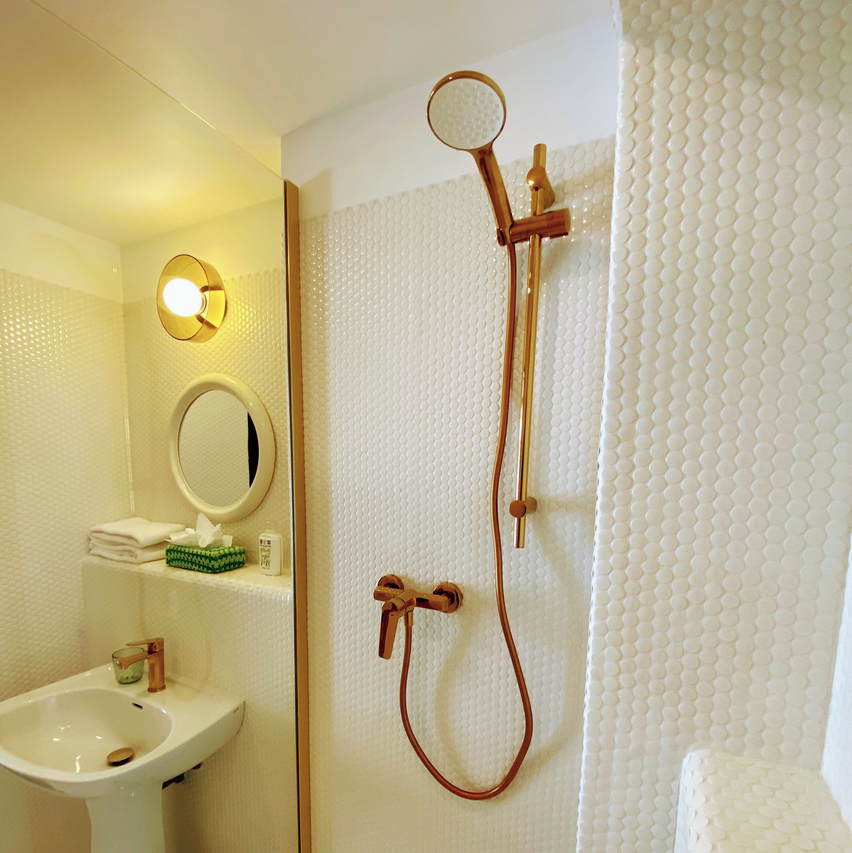 A bathroom with a sink, mirror, and shower with a handheld showerhead.