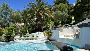 Une piscine avec un jacuzzi, des chaises longues et des parasols.