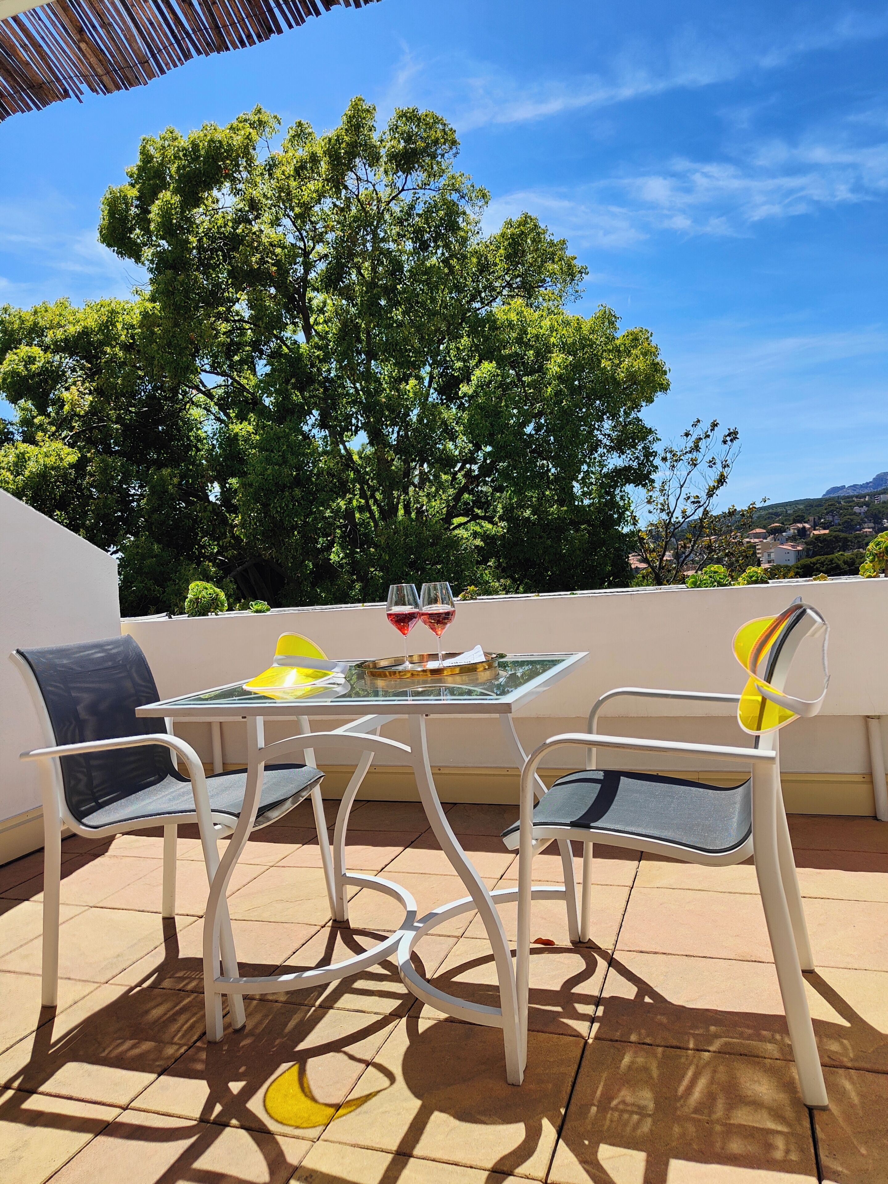 A patio with a table and chairs, a glass top, and two wine glasses.