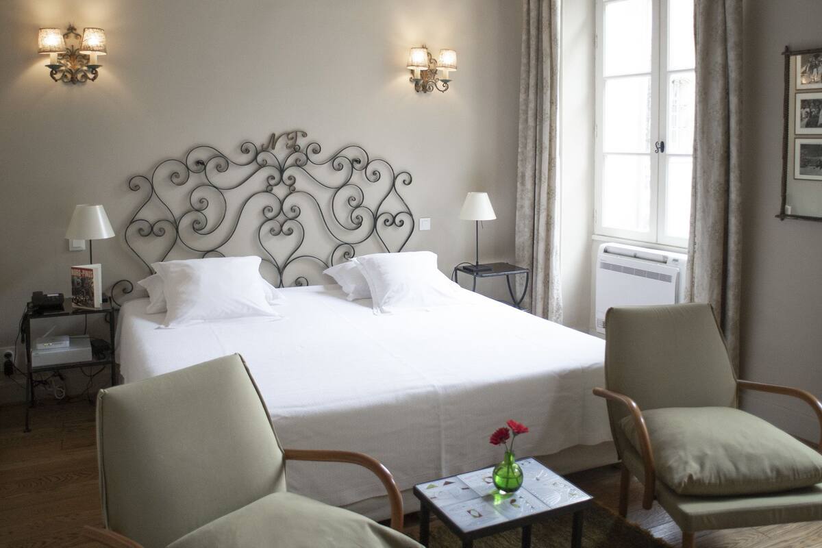 A hotel room with a large bed, two chairs, a small table with a vase, and a ceiling fan.