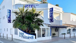 Hotel llamado "Hotel les Palmietts", con un letrero destacado, una palmera en primer plano y un cielo azul despejado.