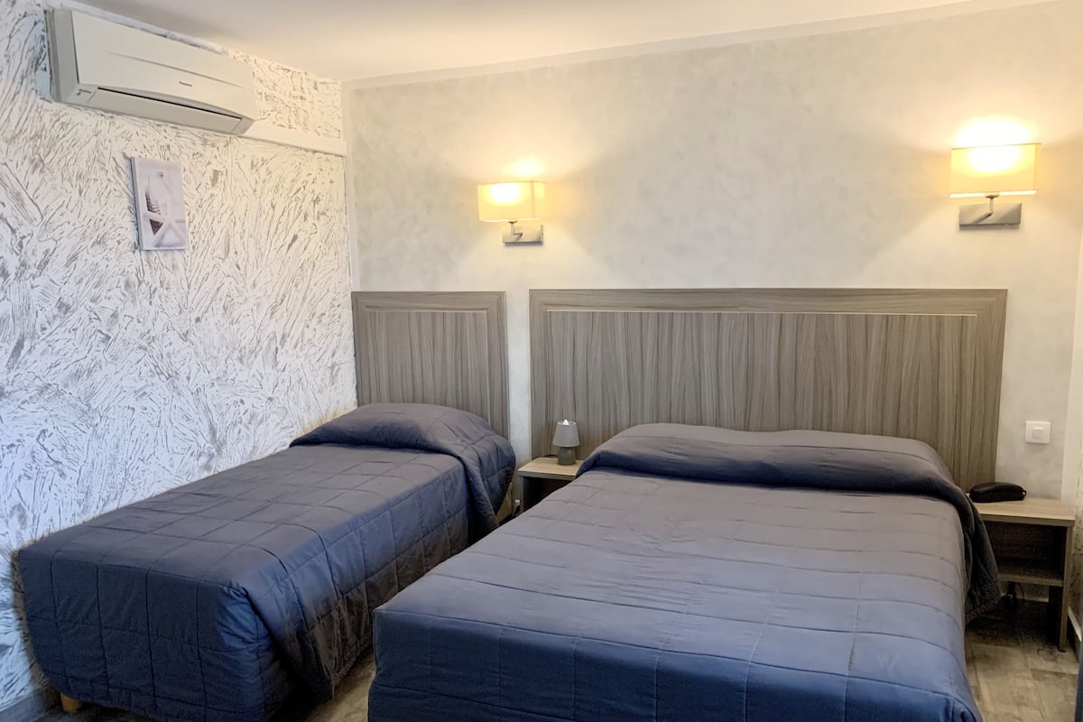 Ein Zimmer mit zwei Betten, einer Wand-Klimaanlage und zwei Nachttischlampen.