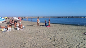 Una playa arenosa con gente tomando el sol y nadando.