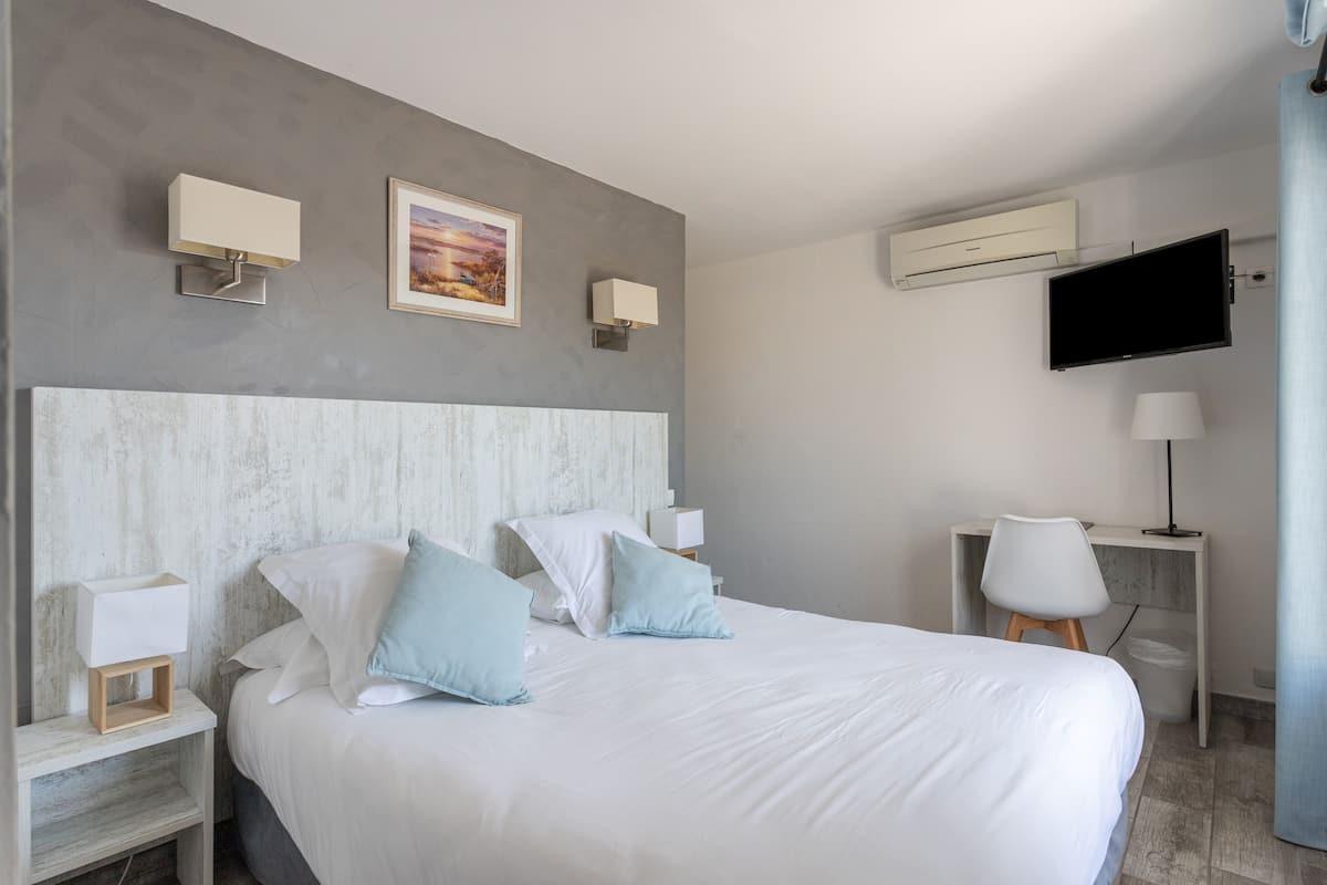 Ein modernes Hotelzimmer mit einem großen Bett, zwei Nachttischen, einem Schreibtisch mit Stuhl, einem Flachbildfernseher und einer Klimaanlage.