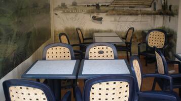A restaurant with outdoor seating featuring tables and chairs with woven backrests.