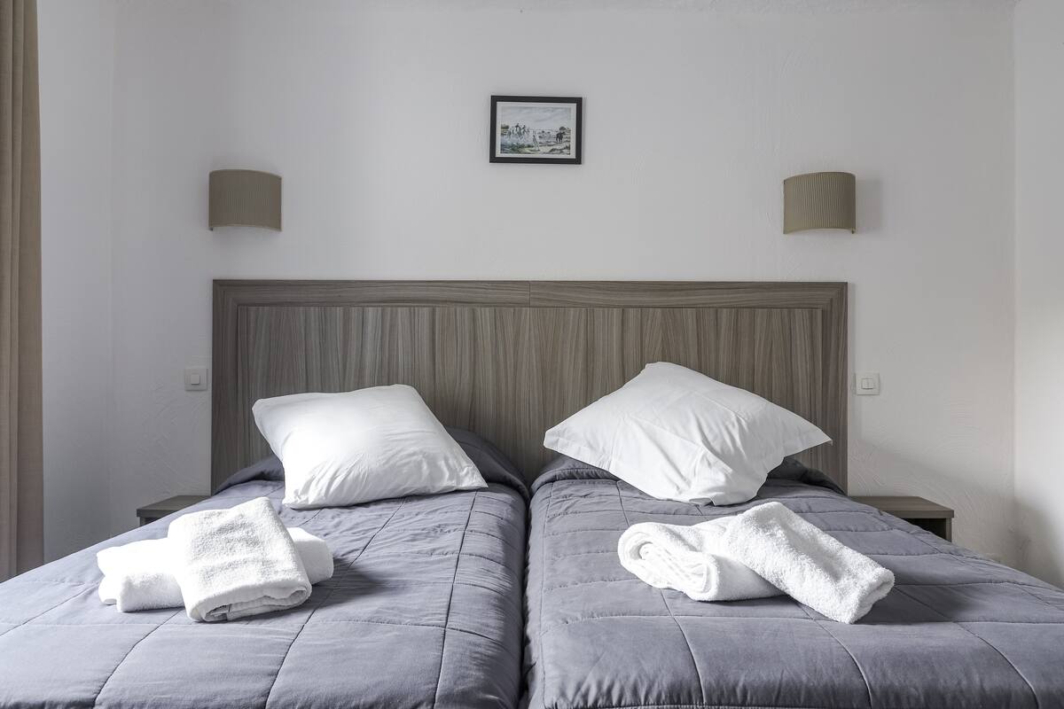 Ein Doppelbett mit grauer Bettwäsche und weißen Kissen, zwei Nachttische und ein gerahmtes Bild an der Wand.