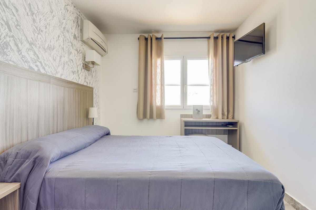 Ein Hotelzimmer mit Bett, Schreibtisch, Fernseher und einem Fenster mit Vorhängen.