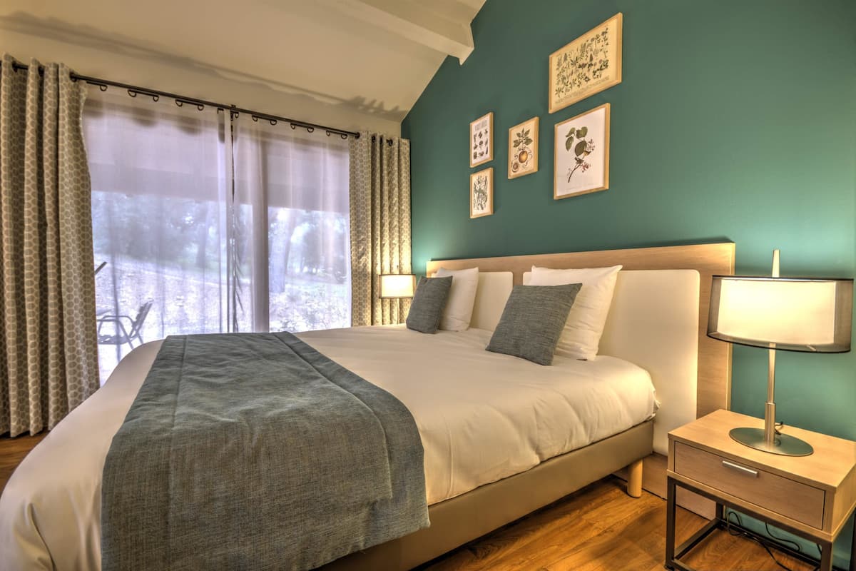 A bedroom with a bed, bedside table, and a window with curtains.