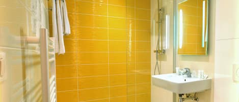 Une salle de bain avec des murs recouverts de carreaux jaunes, une douche en verre, un lavabo blanc et des toilettes.