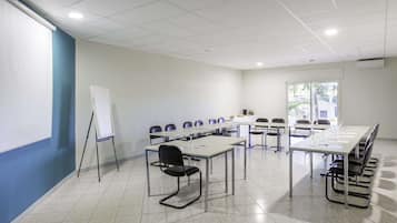 Una sala de conferencias con una pizarra, varias mesas y sillas dispuestas para reuniones.