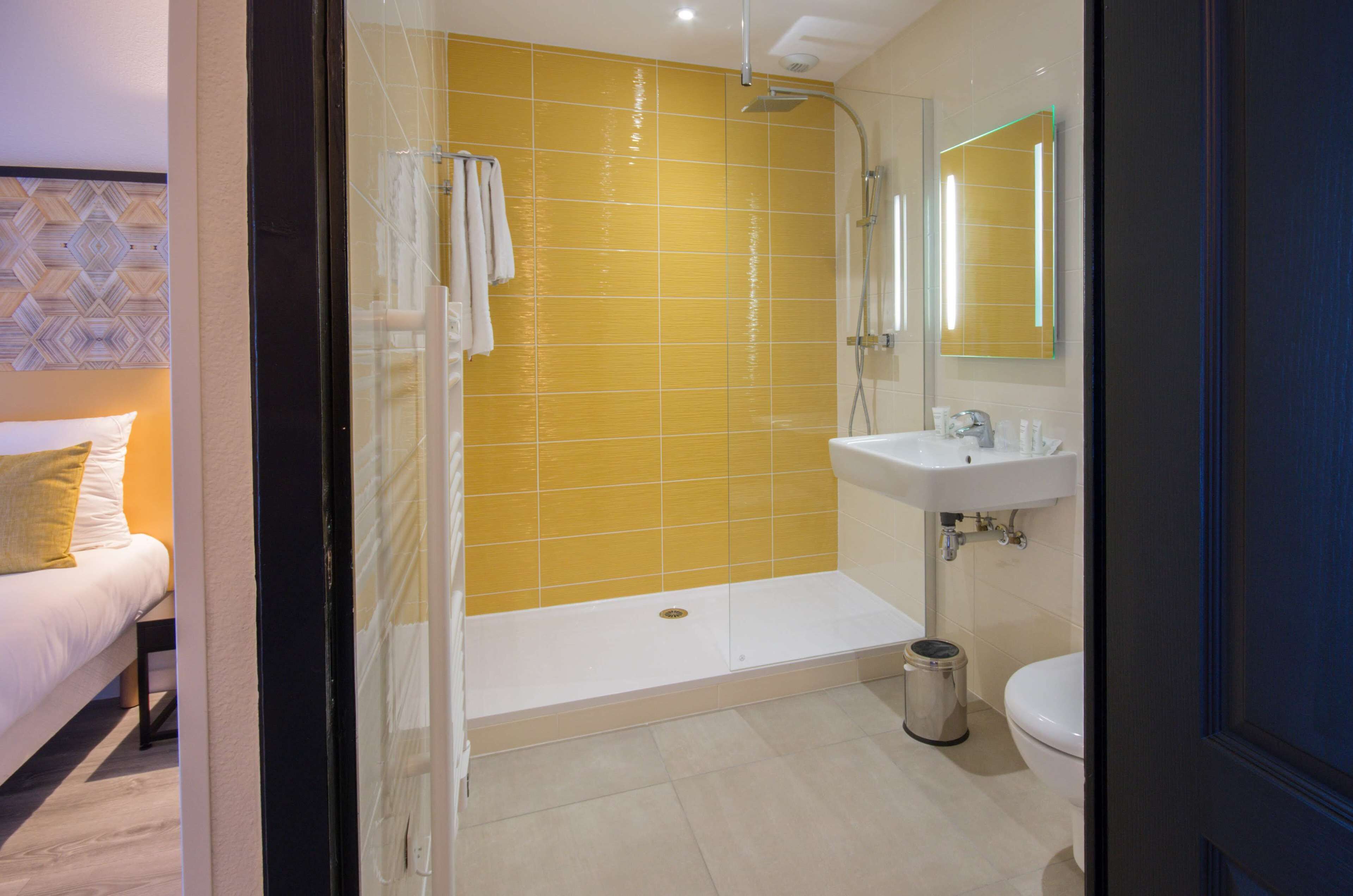 Ein modernes Badezimmer mit einer duschwand aus gelben Fliesen, einem weißen Waschbecken und einer Toilette.