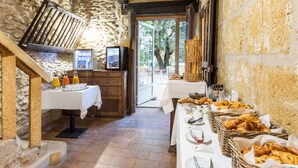 A rustic dining area with stone walls, a wooden staircase, and a buffet table with bread and pastries. - Best Western Domaine de Roquerousse (Salon-de-Provence)