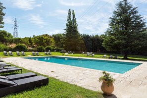 Una piscina rectangular amb solàrium enrajolat, envoltada de gandules i una zona verda.