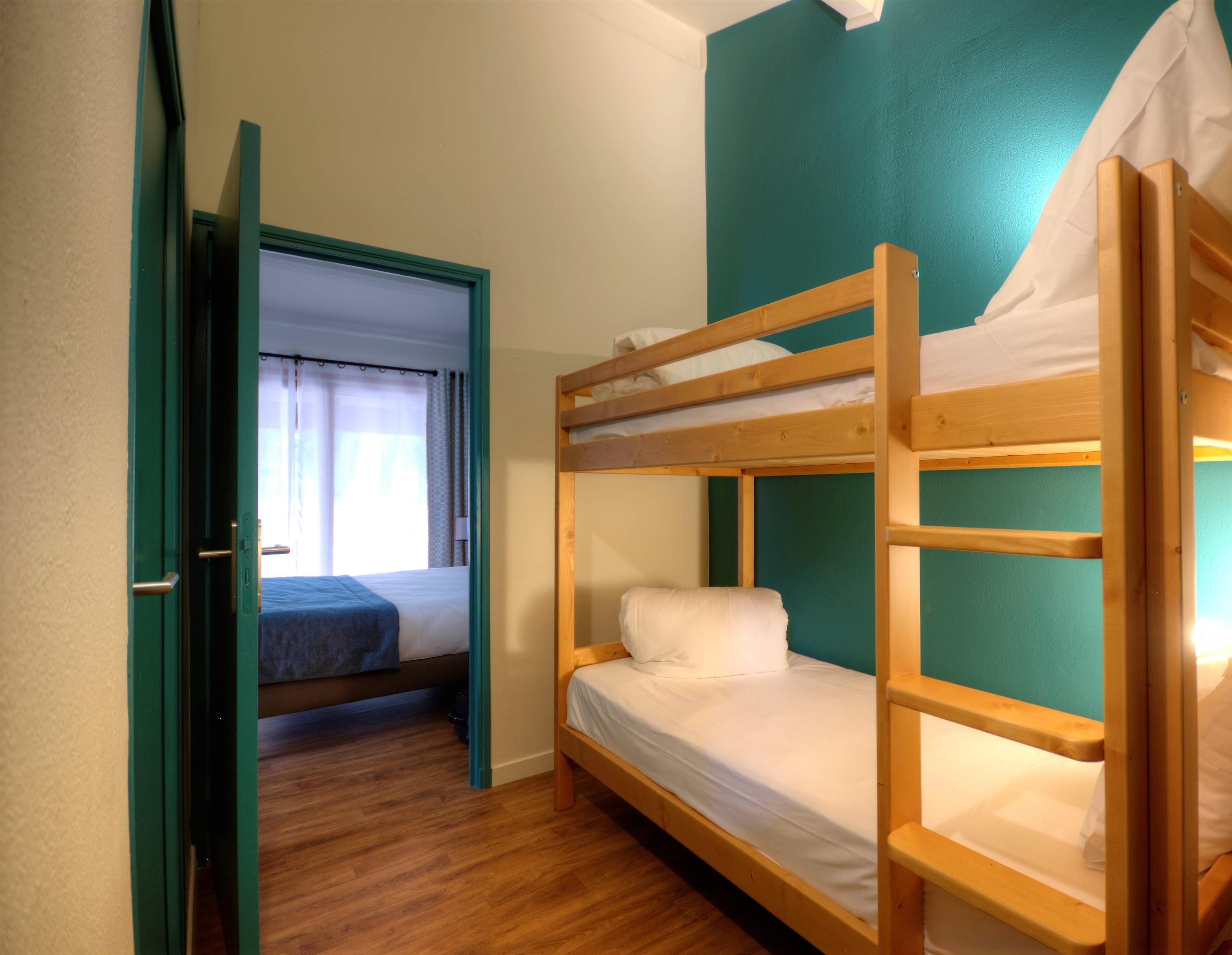 Habitación con literas, suelo de madera y paredes verde azulado.
