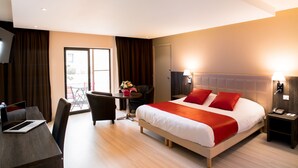A hotel room with a bed, a desk, a chair, a small table with a flower arrangement, and a TV. - Hôtel Ariane (Fos-sur-Mer)