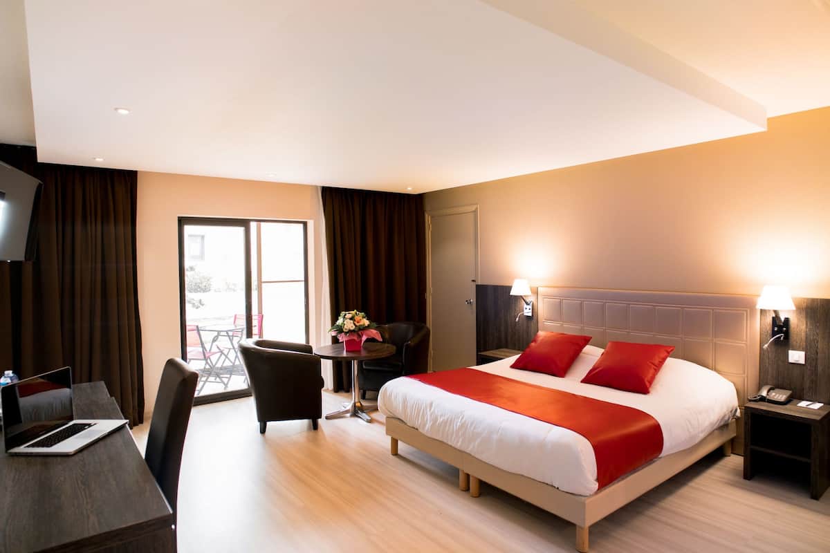 A hotel room with a bed, a desk, a chair, a small table with a flower arrangement, and a TV.