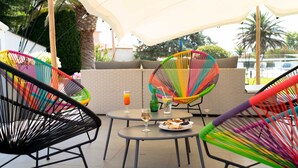 A patio area with colorful woven chairs, a round table with drinks and snacks, and a white canopy. - Hôtel Ariane (Fos-sur-Mer)