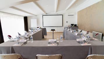 Una sala de conferencias con una larga mesa, sillas, una pantalla de proyector y una pizarra.