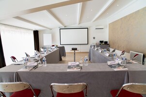 Una sala de conferencias con una larga mesa, sillas, una pantalla de proyector y una pizarra.
