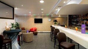 A bar area with a counter, seating, a television, and a wall of liquor bottles. - Hôtel Ariane (Fos-sur-Mer)