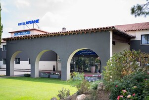 Un hotel llamado "Hotel Ariane" con una fachada moderna, arcos y un jardín bien cuidado.