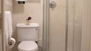 A bathroom with a toilet, a shower enclosure, and a small shelf with a towel. - Celtic Lodge Guesthouse - Restaurant & Bar (Dublin)