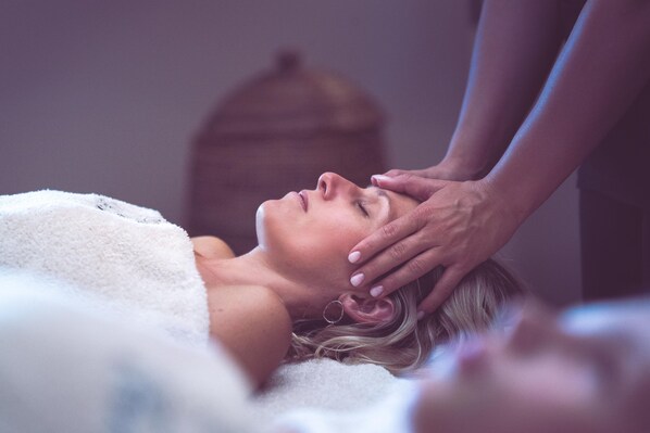 A person receiving a massage in a room with a wooden headboard and a white blanket.