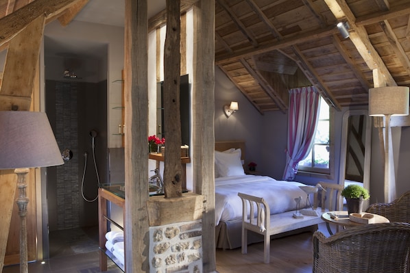 Un dormitorio con techo de madera, una cama, una mesita de noche, una lámpara, una silla y una pequeña mesa con una planta.