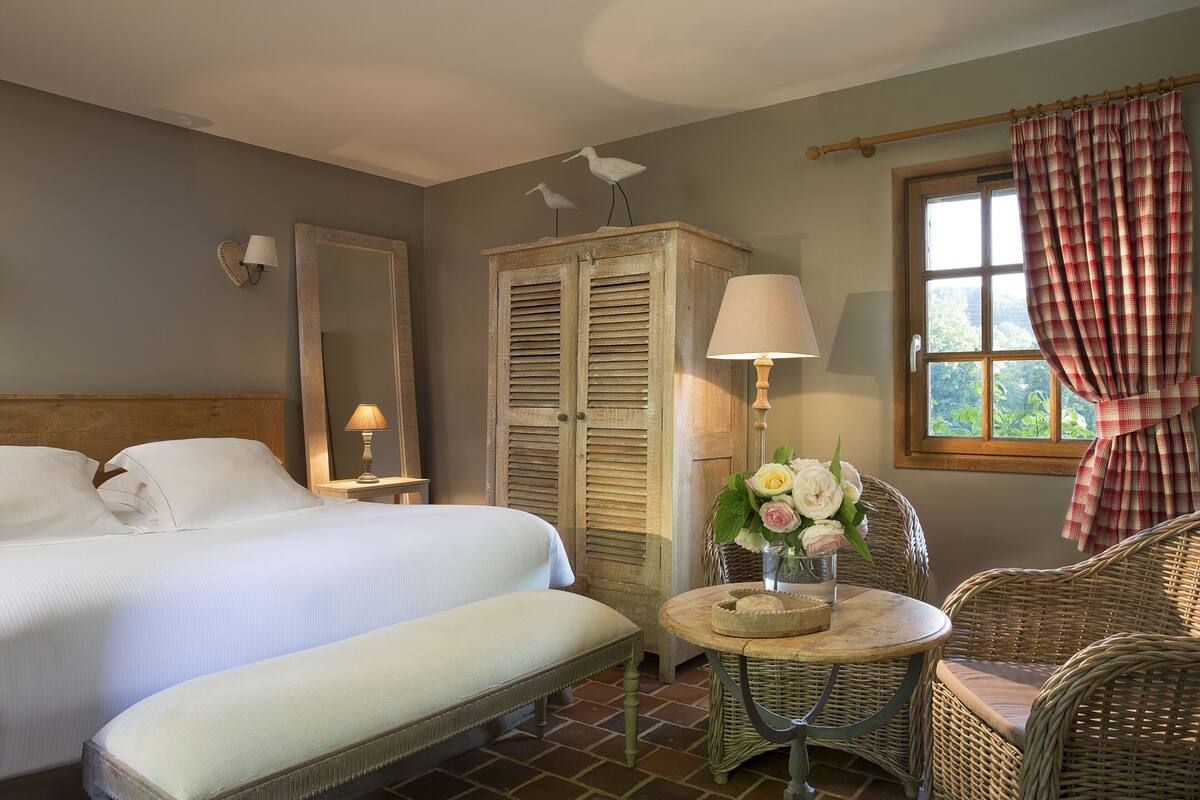 A bedroom with a bed, bedside table, lamp, and a wicker chair.