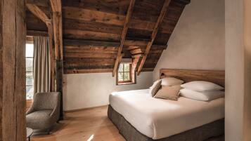 A bedroom with a wooden ceiling, a bed with white bedding, a chair, and a window.