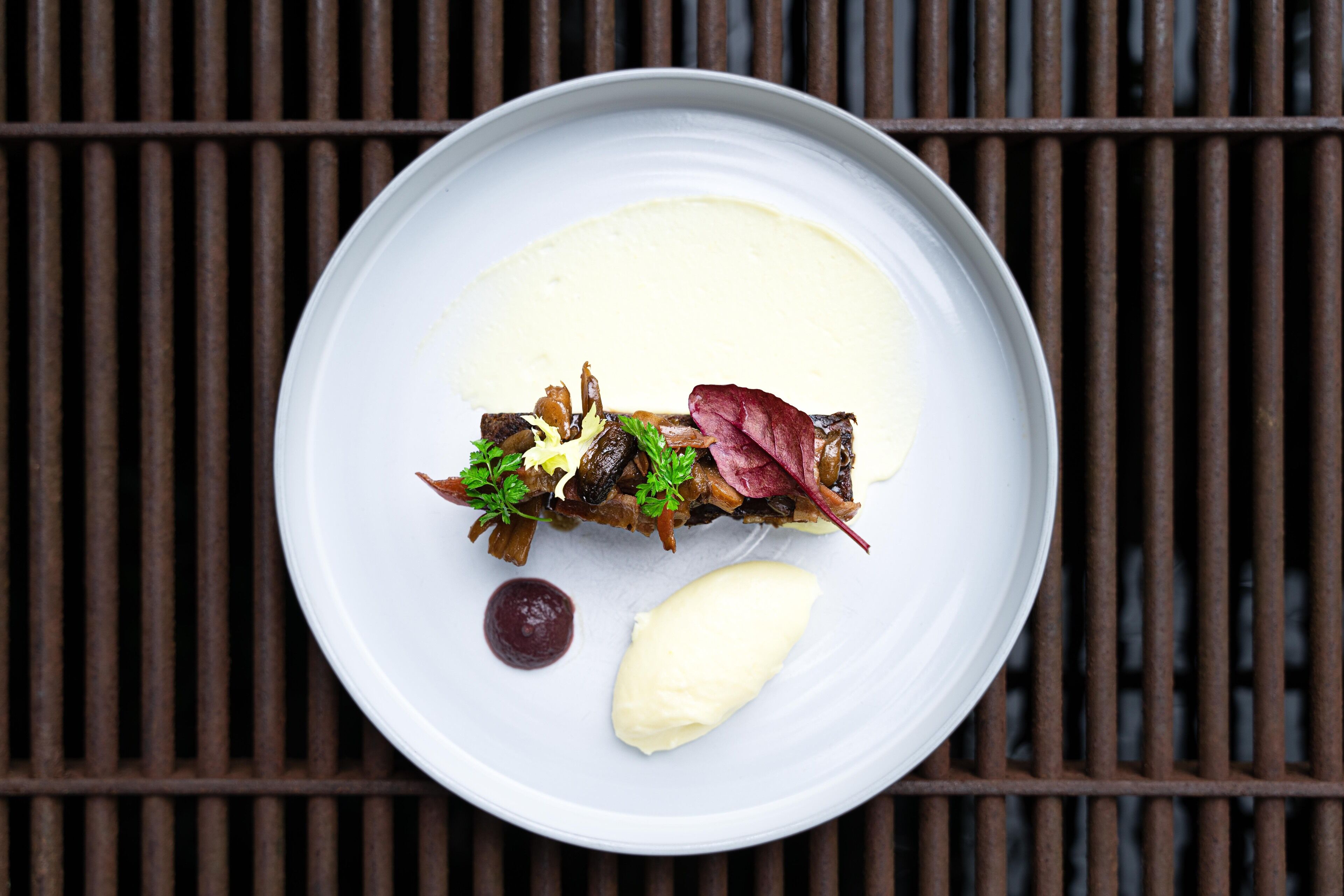 Une assiette blanche contenant un plat de viande, des légumes et une cuillerée de sauce, le tout posé sur une grille métallique.